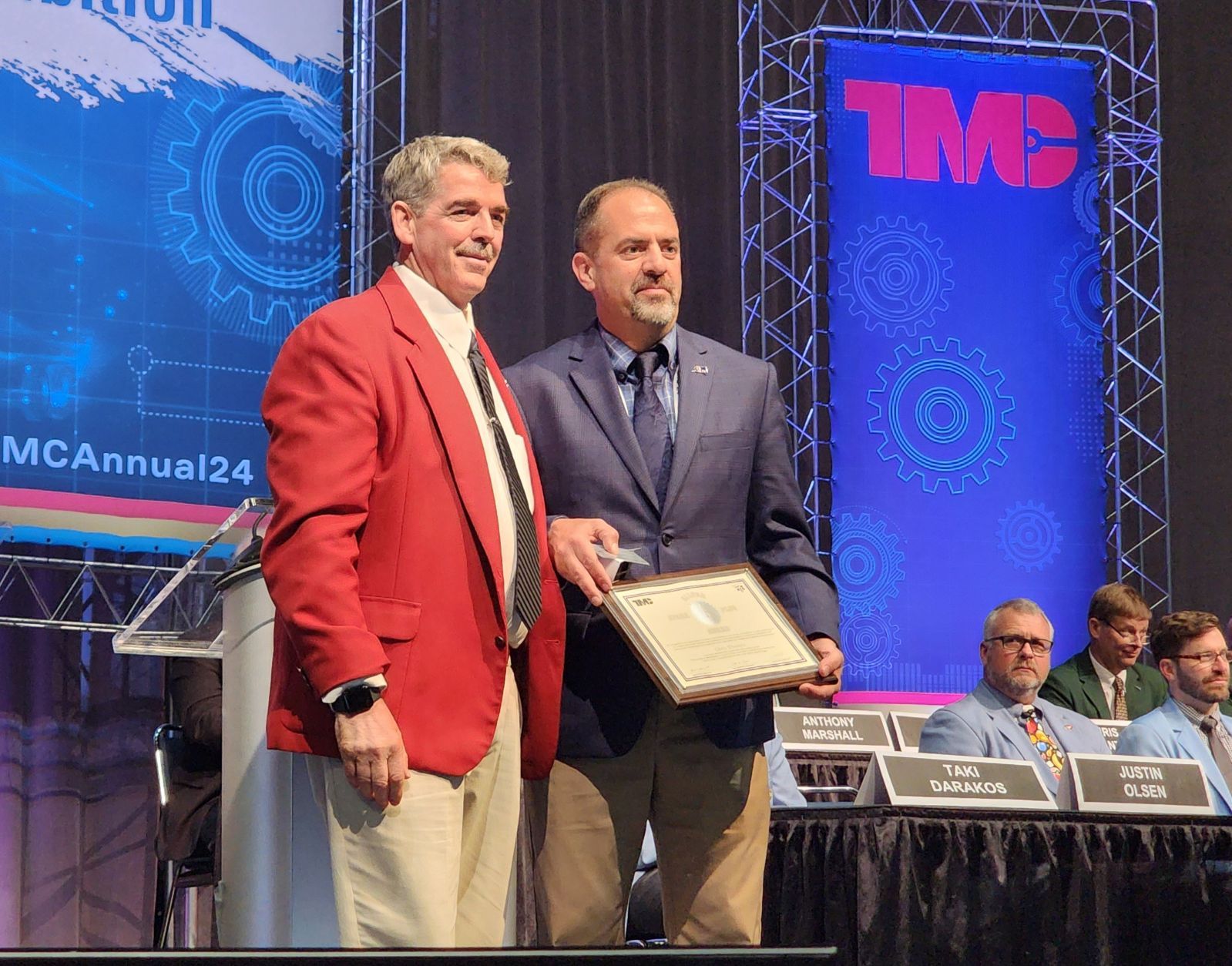 Chris Disantis Poses on stage holding TMC's Coveted Silver Spark Plug Award